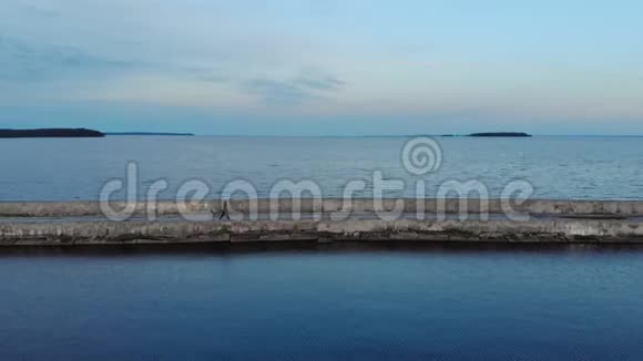 一个穿着黑色衣服的人在一个美丽的蓝色湖泊上空的防波堤上散步鸟瞰视频的预览图