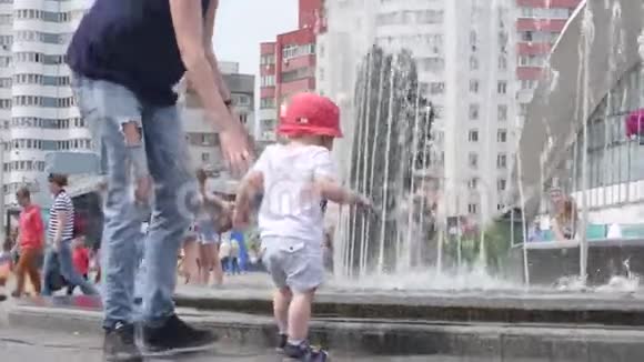年轻女子牵着她的小儿子的手靠近喷泉向她的男孩展示了市中心的落水视频的预览图