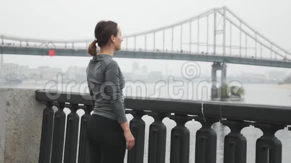年轻漂亮的运动装女人在跑步训练前正在城市码头上伸展穿漂亮衣服的黑发女子视频的预览图