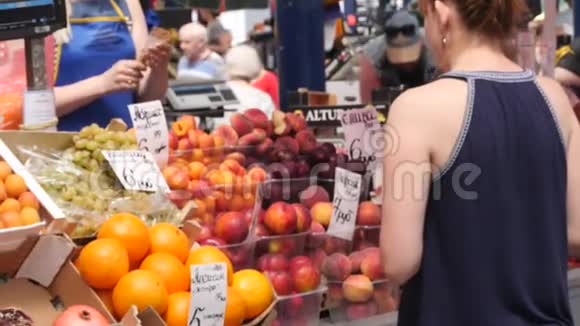 美丽的女人在城市市场买水果不可辨认的女卖家给她买回头看慢视频的预览图