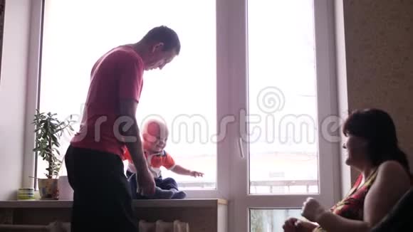 年长的男人和女人正在和坐在窗台上的可爱的小孙子玩耍祖母吓了一跳视频的预览图