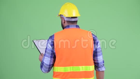 年轻超重留胡子的印度男子建筑工人拿着剪贴板和指挥的后视图视频的预览图