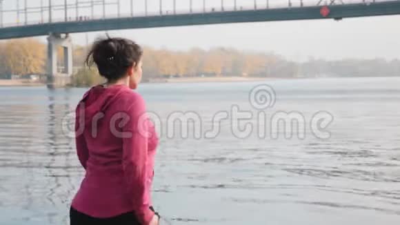 在后侧沿着年轻胖乎乎的女孩的视线独自在河和城市公园里做晨间北欧散步运动视频的预览图