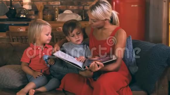 一位年轻的母亲和两个孩子坐在沙发上孩子们在厨房的背景下他们看书微笑着视频的预览图