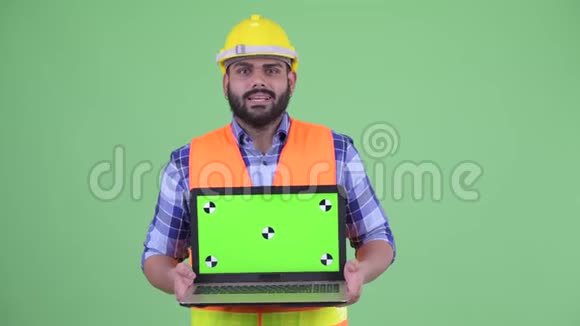 快乐的年轻超重留着胡子的印度工人一边说话一边拿着笔记本电脑视频的预览图