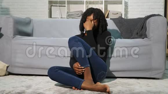 穿套头衫和牛仔裤的黑人女孩坐在沙发的白色地板上视频的预览图