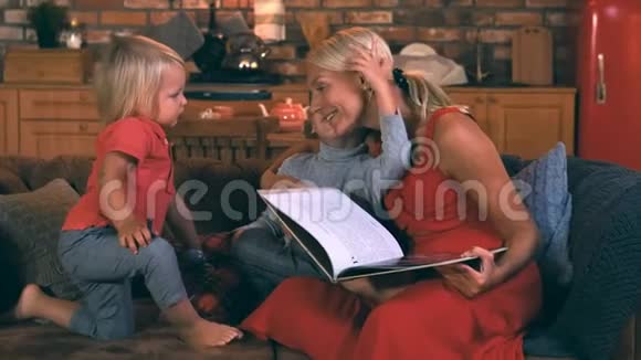 一位年轻的母亲坐在沙发上两个孩子男孩手里拿着一本书一个哥哥在她耳边说些什么视频的预览图