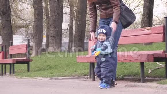 一个年轻的女人和她的小男孩抱着小铲子走在城市公园里在一个春天的阴天和孩子视频的预览图