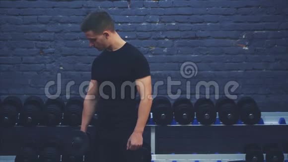 穿黑色T恤的小男孩健身房里的一个大杠铃经常在黑暗的背景上训练手视频的预览图