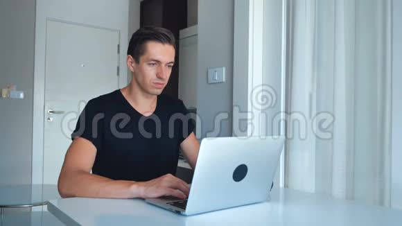 年轻的男性自由职业者使用笔记本电脑处理图像并在家里喝咖啡视频的预览图