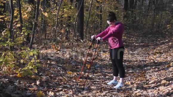 胖女人在秋季公园的北欧步行训练前伸展背部和臀部健身理念视频的预览图