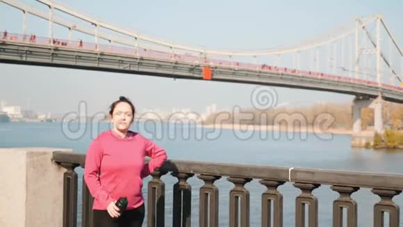 年轻胖乎乎的女性在城市公园进行强化跑步和北欧步行训练后喝水水化概念视频的预览图