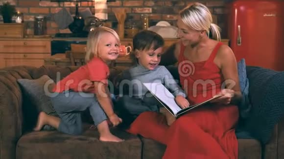 美丽的母亲读了一本书给两个儿子他们坐在厨房的沙发上带着微笑的男孩视频的预览图