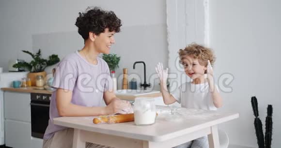 淘气的男孩拍着脏手沾满面粉和妈妈在家做饭视频的预览图