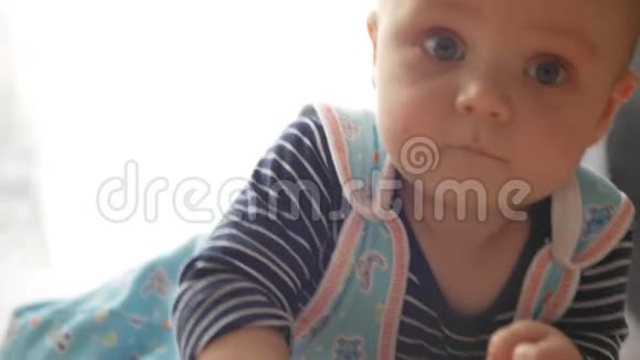 婴儿男孩正看着相机试图爬到他的肚子上用手抓住它慢动作视频的预览图