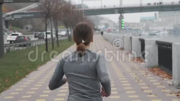 瘦小的年轻女子与美丽的身体快速运行在城市码头沿河和桥的背景女运动员准备视频的预览图