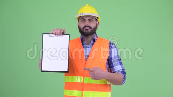 快乐年轻超重留胡子的印度男建筑工人展示剪贴板并竖起大拇指视频的预览图