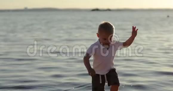 可爱的男孩在日落时走在湖岸上视频的预览图