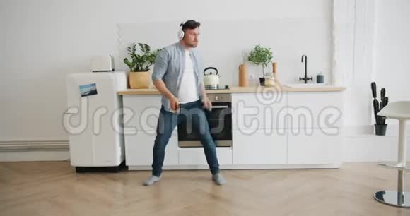 戴着耳机的男人在厨房里跳舞拿着智能手机在家里玩得开心视频的预览图