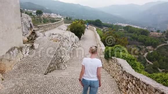 金发女人走在欧洲山脉中世纪城堡的防御墙上视频的预览图