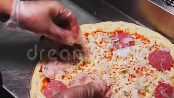 戴手套的人把火腿片放到厨房的生披萨上视频的预览图