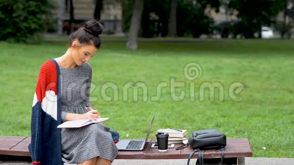 美丽的年轻女孩学生正在户外公园的笔记本上写作视频的预览图