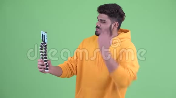 快乐年轻体重超重留着胡子的印度男人一边打电话视频的预览图