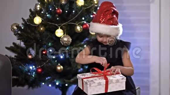 小白种人女孩坐在圣诞树附近用一些特别的东西打开她的礼物假日和庆祝活动视频的预览图