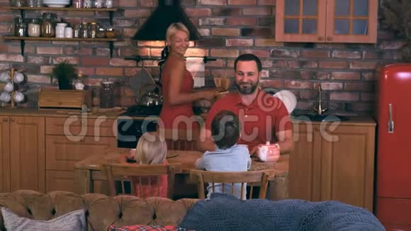 友好的家庭爸爸妈妈和两个孩子聚集在餐桌前妈妈为晚餐烤了一个馅饼视频的预览图