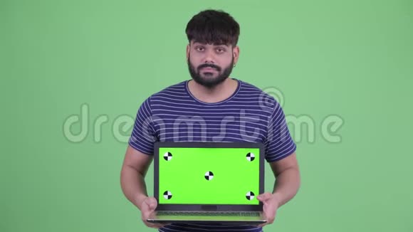 穿着年轻超重留着胡须的印度男人展示笔记本电脑并得到坏消息视频的预览图