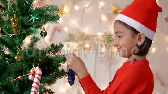 一个戴着红色圣诞帽的可爱小女孩正在装饰一棵圣诞树视频的预览图