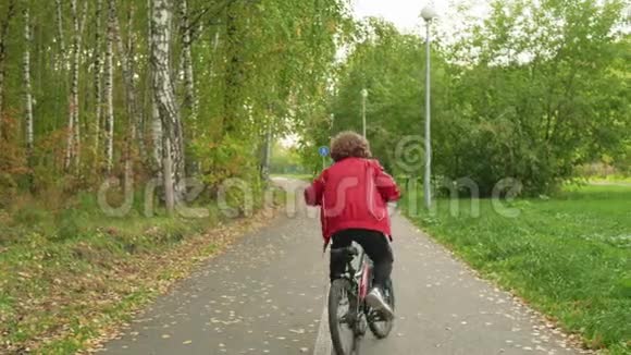 小男孩骑自行车在城市公园的道路上骑自行车在夏日后景骑自行车的快乐男孩骑自行车视频的预览图