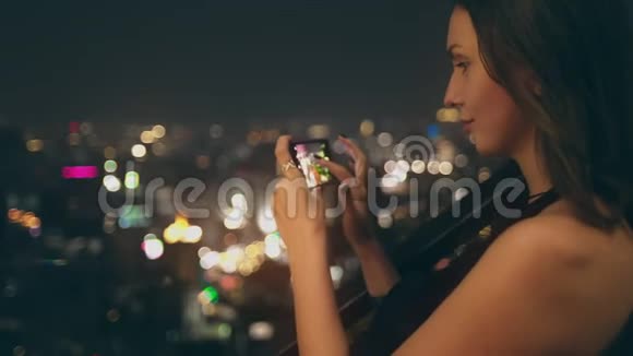 美女在城市之夜用手机拍视频视频的预览图