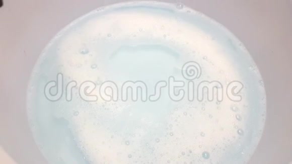 一只雌性的手把脏东西放在蓝色的盆里里面有水和白色的泡泡用洗涤剂洗脏衣服视频的预览图