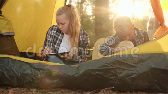 夏天徒步旅行露营帐篷里的十几岁男孩和女孩女孩在笔记本上画画在里面弹吉他的男孩视频的预览图