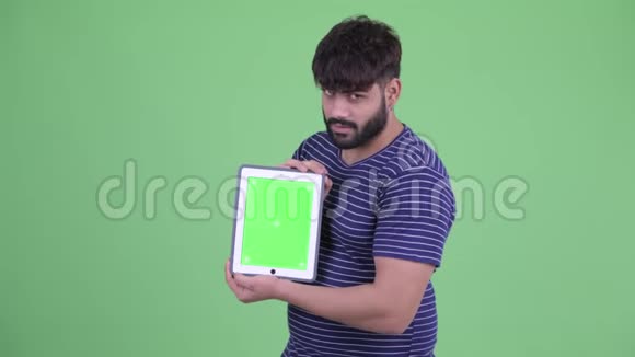 快乐年轻体重超重留着胡须的印度男人展示数码平板电脑并获得好消息视频的预览图