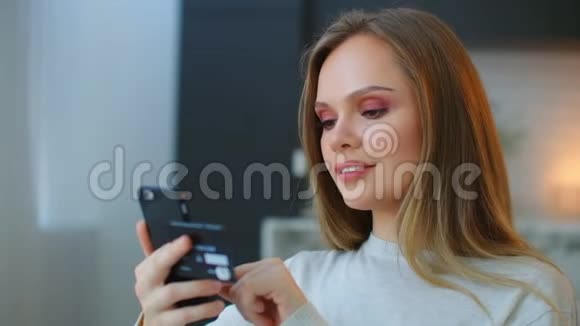 一个快乐微笑的女人手里拿着一部智能手机用手机银行在线购买购买网上礼品视频的预览图