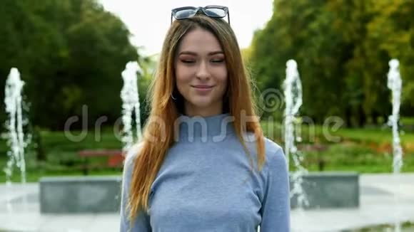 在背景的喷泉公园里一个快乐美丽的红发女人看着摄像机的特写肖像视频的预览图