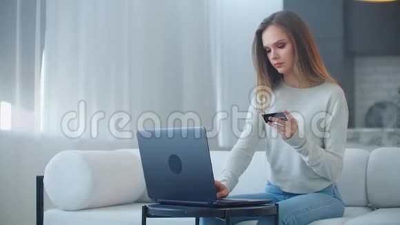 一个年轻漂亮的金发女人看着笔记本电脑屏幕手里拿着一张银行卡使用银行服务视频的预览图