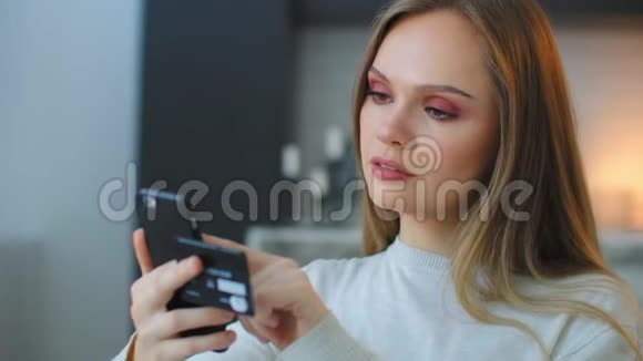 一位年轻漂亮的女士拿着一部智能手机和一张信用卡同时支付购买费用并进入一个支付密码视频的预览图