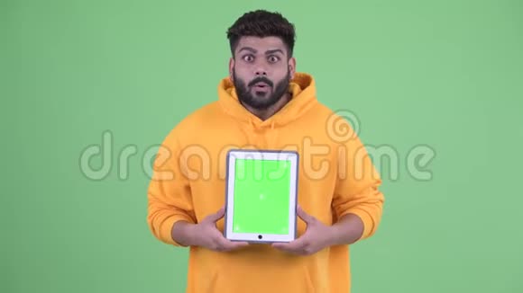 年轻快乐体重超重留着胡须的印度男人展示数码平板电脑看上去很惊讶视频的预览图