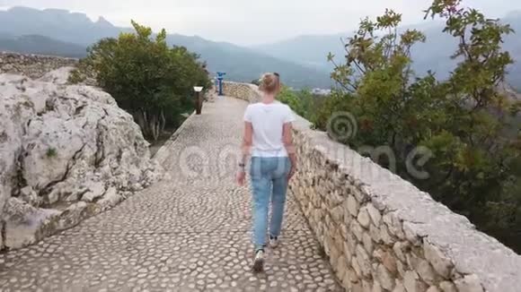 金发女孩走在欧洲山脉中世纪城堡的防御墙上视频的预览图
