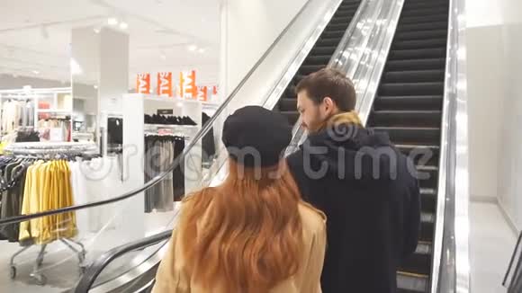 快乐的年轻白种人夫妇手里拿着购物袋站在自动扶梯上视频的预览图