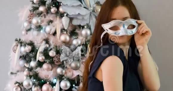 戴着狂欢面具的红长发的女人在圣诞树附近亲吻视频的预览图