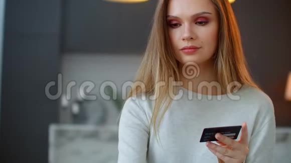一个漂亮的金发女人看着笔记本电脑屏幕拿着银行卡家庭网上购物视频的预览图