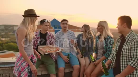 六个年轻人的公司在屋顶上用披萨和啤酒互相交流女孩们看着夏天视频的预览图