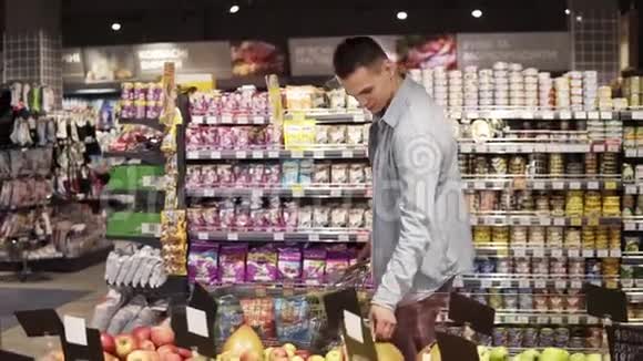 一个面带笑容的白种人穿着蓝色衬衫在一家杂货店的食品部买水果和蔬菜视频的预览图
