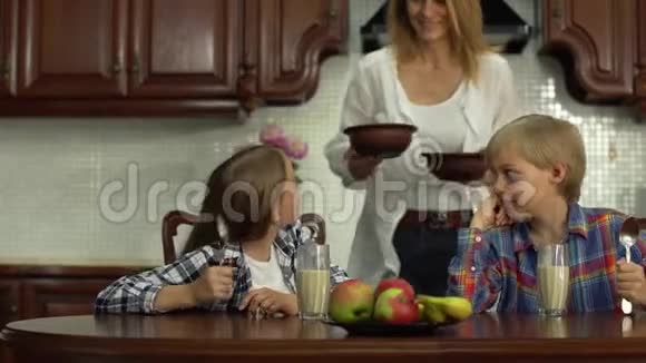 快乐的母亲在早上放学前喂孩子微笑着兄弟姐妹在餐桌上吃麦片和喝牛奶视频的预览图