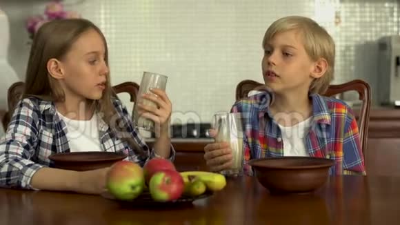 可爱的孩子从眼镜里喝牛奶小兄弟在厨房的餐桌旁享用健康的饮料视频的预览图