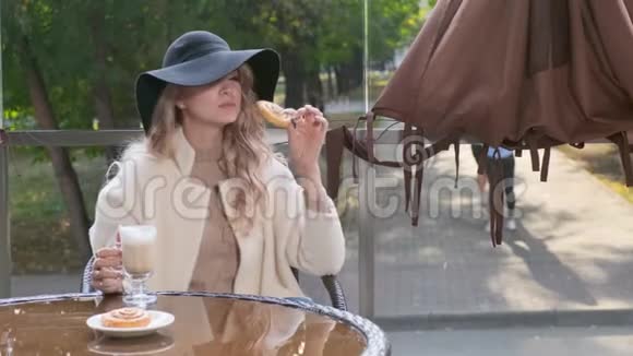 优雅的女人戴着黑帽子在街头咖啡馆里吃着甜糕点蛋糕视频的预览图